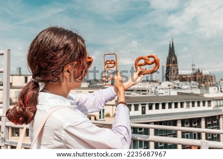 Happy tourist girl taking photo with a pretzel and Cologne cathedral building on the background. Travel and tourism in Germany and Rhineland Royalty-Free Stock Photo #2235687967