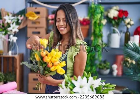 Young hispanic woman florist holding bouquet of flowers at florist store Royalty-Free Stock Photo #2235689083