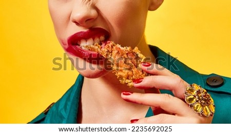 Cropped image of woman in green coat with red lipstick smudge, eating fried chicken, nuggets over yellow background. Spicy taste. Food pop art photography. Complementary colors. Copy space for ad