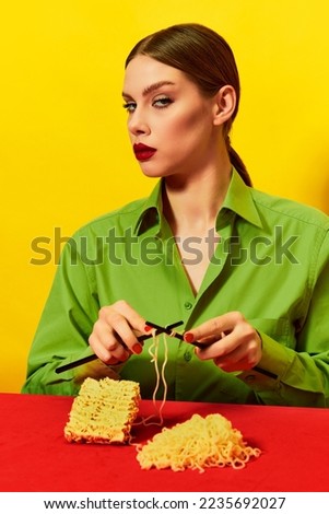 Woman with emotionless face knitting instant noodles on blue table on vivid red tablecloth over yellow background. Food pop art photography. Complementary colors. Copy space for ad, text