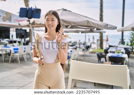 Young chinese girl smiling happy having video call using smartphone at the promenade.