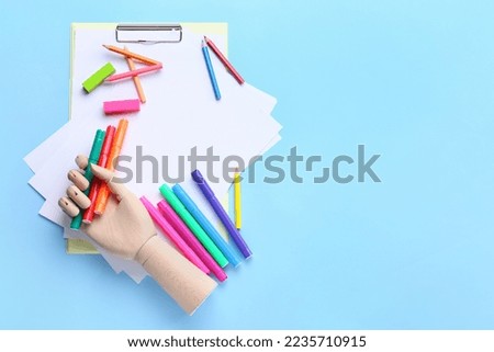 Blank paper sheets with wooden hand, felt-tip pens, pencils and erasers on blue background