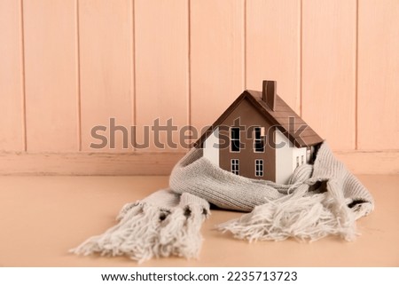 House model with scarf on beige wooden background. Heating concept