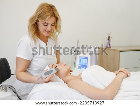 Cosmetologist aesthetist performs the procedure of ultrasonic facial cleansing. Horizontal photo