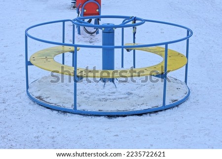 childrens playground with a one round blue yellow carousel stands on white snow on a winter street