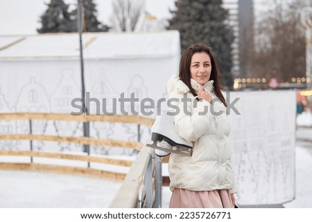 Attractive stylish young brunette holding ice skates near skating rink. Winter activities.