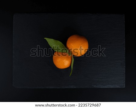 Two ripe mandarins with green leaves on a black stone plate. Dark background.  Top view. Copy space. Royalty-Free Stock Photo #2235729687