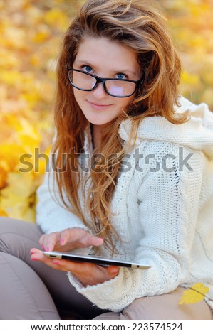 Girl in glasses with a tablet in hands in a park in autumn