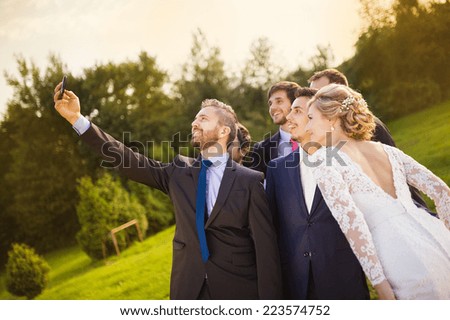 Outdoor portrait of beautiful young bride with groom and his friends taking selfie
