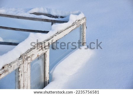Wooden boxes in winter in the snow. A small greenhouse in snowdrifts in winter.Farming agriculture concept.