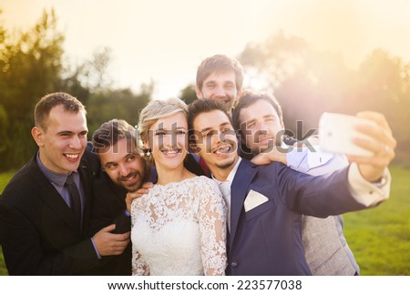 Outdoor portrait of beautiful young bride with groom and his friends taking selfie