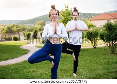 Teenager boy with yoga instructor doing vrikshasana outside on grass while standing in park. Maintaining healthy lifestyle. Summer sport concept