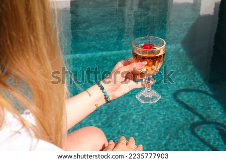 Lifestyle summer concept. Beautiful blonde woman holding rose or blush wine glass on pool background. Royalty-Free Stock Photo #2235777903