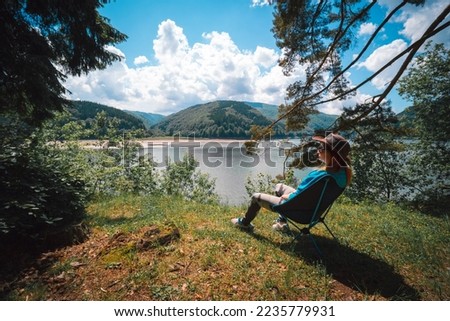 Girl enjoy the view on the mountain overlooking the lake. They sit on folding portable camping chairs. Concept of equipment for tourism and vacation. Active lifestyle. Tereblya, Ukraine Royalty-Free Stock Photo #2235779931