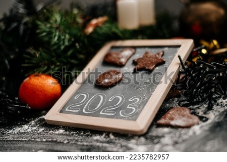 New Year sign 2023. Baking Christmas gingerbread cookies on a dark wooden table. Christmas lights in background. Winter holidays. Top view. Shallow depth of field. 