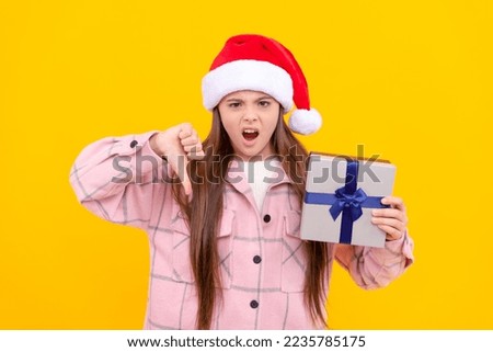 unhappy teen girl in santa claus hat dislike present box on yellow background, boxing day