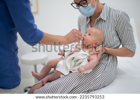 Pediatrician administring oral vaccination against rotavirus infection to little baby in presence of his mother. Children health care and disease prevention. Royalty-Free Stock Photo #2235793253