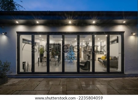 Stylish, modern, designer kitchen diner room in white and grey with sofa, couch shown through bifold doors. Night, evening shot with Christmas, Xmas tree. Royalty-Free Stock Photo #2235804059