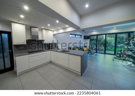 Stylish, modern, designer kitchen diner in white and grey with sofa, couch and beautiful garden showing through bifold doors. With Christmas, Xmas tree. Royalty-Free Stock Photo #2235804061