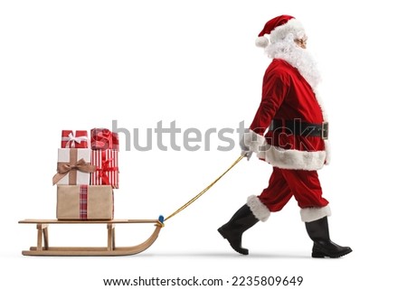 Full length profile shot of santa claus pulling a wooden sled with presents isolated on white background