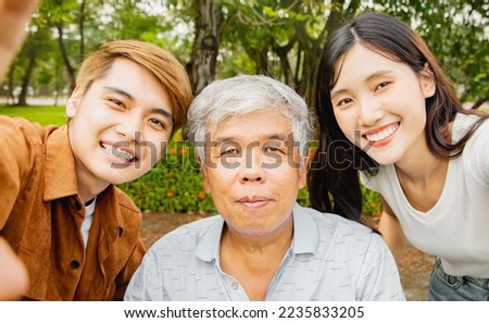 Portrait asian family of three, aged father, son and daughter showing smiling good mood happy taking pictures with healthy father in the park : Health insurance for the retired elderly concept.