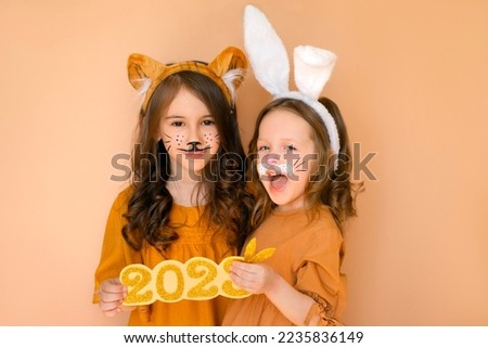 A girl dressed as tiger and sister in the guise of rabbit, two symbols of outgoing year and new year, hold golden number 2022