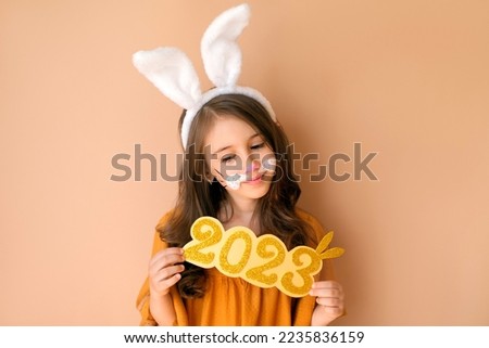 Cute beautiful girl with bunny ears dressed up as a hare with a thoughtful look holds the golden numbers 2022. New Year of the Rabbit