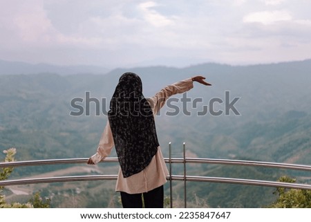 Woman wearing hijab taking pictures with her back in a tourist attraction in Thailand