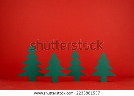 Holiday Christmas background in minimal style with paper green spruces in row on red backdrop, mockup for presentation of gifts, goods and advertising, design of card, flyer, poster, copy space.