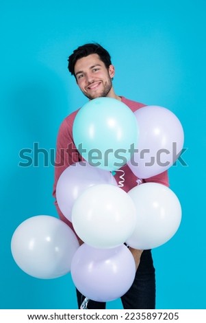Positive Caucasian Guy Handsome Brunet Man With Bunch of Colorful Air Balloons in Pink Jumper Against Blue Background. Vertical image