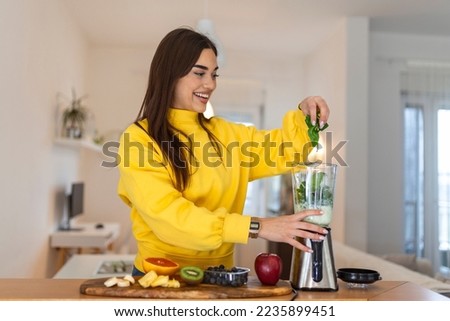 Young woman making smoothie with fruits. Beutiful girl standing in the kitchen and preparing smoothie with fruit and vegetables
