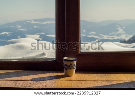 Close up cup on window sill concept photo. Cozy morning. Front view photography with snowy winter landscape on background. High quality picture for wallpaper, travel blog, magazine, article