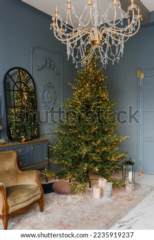 Classic living room with blue walls. Christmas decor in the house. Christmas tree near the chair and mirror