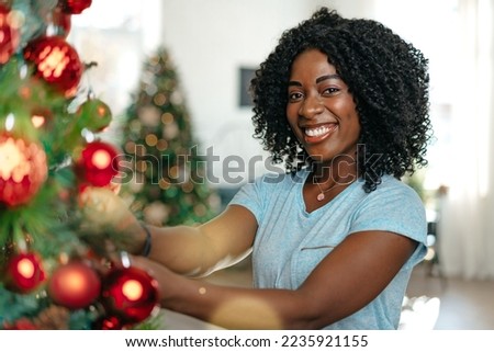 Beautiful young african woman decorating Christmas tree at home