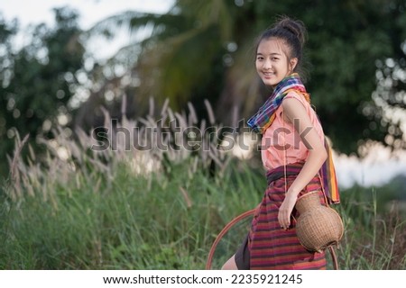 A young Asian farmer girl (with braces) smiling cheerfully as she prepares to fish in a pond beside the rice field. Royalty-Free Stock Photo #2235921245
