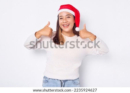 Portrait of smiling young Asian woman in Santa Claus hat showing thumbs up isolated over white background. celebration Christmas holiday and New Year concept