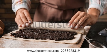 Woman preparing tasty poppy seed strudel at kitchen table, closeup