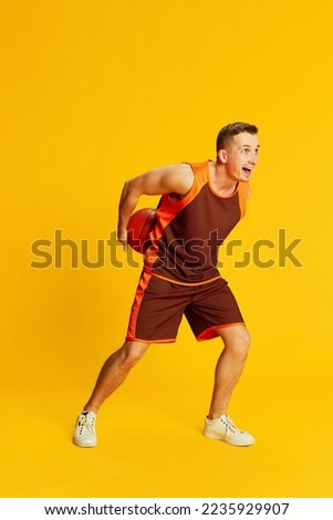 Portrait of young active man in orange uniform training, playing basketball isolated over yellow background. Concept of sport, fitness lifestyle, body care, health, youth, action. Ad