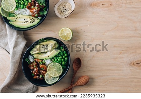 Buddha bowl with crispy sesame chicken asian style. Sweet and sour fried chicken with steamed rice, peas and acocado Royalty-Free Stock Photo #2235935323