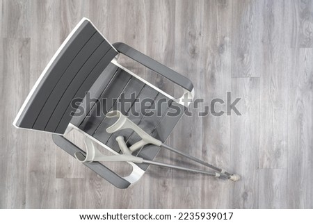 Top view of a plastic chair with medical elbow crutches resting on it. Everything is in grey. Background.