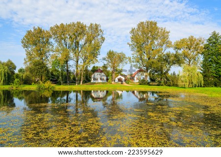 Lake with traditional cottage houses on shore in Radziejowice village on sunny summer day, Poland 