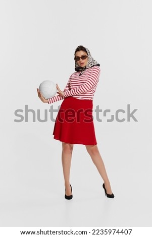 Portrait of beautiful stylish young woman in striped shirt posing with volleyball ball isolated over white background. Concept of summer holidays, retro fashion, vintage style. Copy space for ad