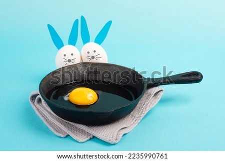 Two funny easter bunny looking into a pan with an egg, holiday greeting card, spring season