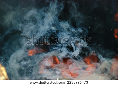 Flames and smoke from open fire fireplace outdoor in the forest. Burning wood at night. Campfire at touristic camp in nature in mountains. Smoke on dark abstract background.