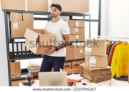Young hispanic man working at small business ecommerce smiling looking to the side and staring away thinking. 