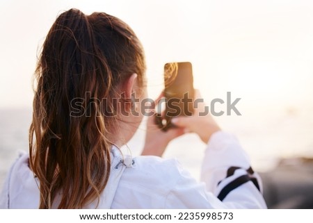 Woman, back or phone picture of beach sunset by ocean or sea in nature environment, holiday vacation or Canada travel location. Student, tourist or influencer on mobile photography technology or vlog