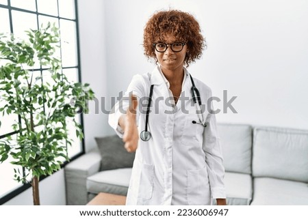 Young african american woman wearing doctor uniform and stethoscope smiling friendly offering handshake as greeting and welcoming. successful business. 