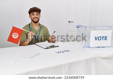 Young arab man smiling confident holding tunisia flag working at electoral college