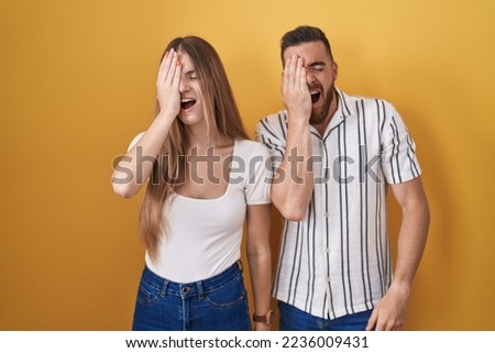 Young couple standing over yellow background yawning tired covering half face, eye and mouth with hand. face hurts in pain. 