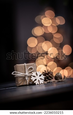 Defocused Image Of Illuminated Christmas Tree Against Black Background. sustainable gift on the foreground
